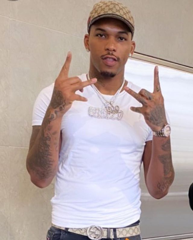 600Breezy is wearing a white tee and and a dark blue jeans.