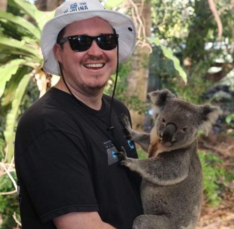 Shane Gillis posing for a photo shoot while holding a Koala bear.
